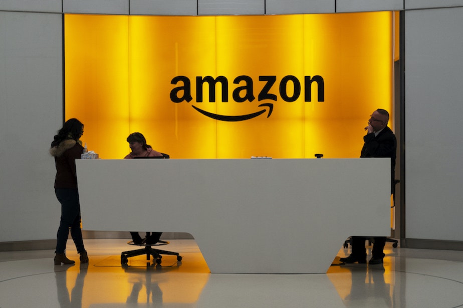 caption: In this Feb. 14, 2019, file photo, people stand in the lobby for Amazon offices in New York.
