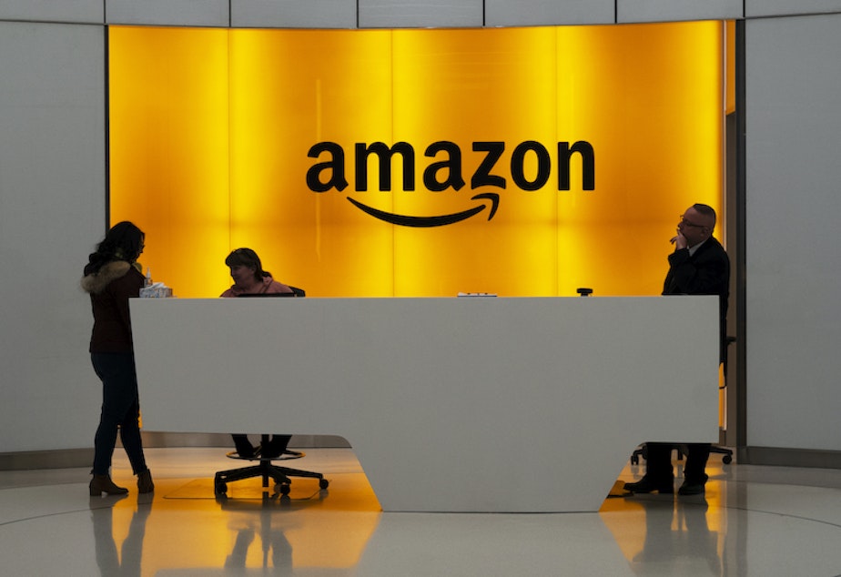 caption: In this Feb. 14, 2019, file photo, people stand in the lobby for Amazon offices in New York.