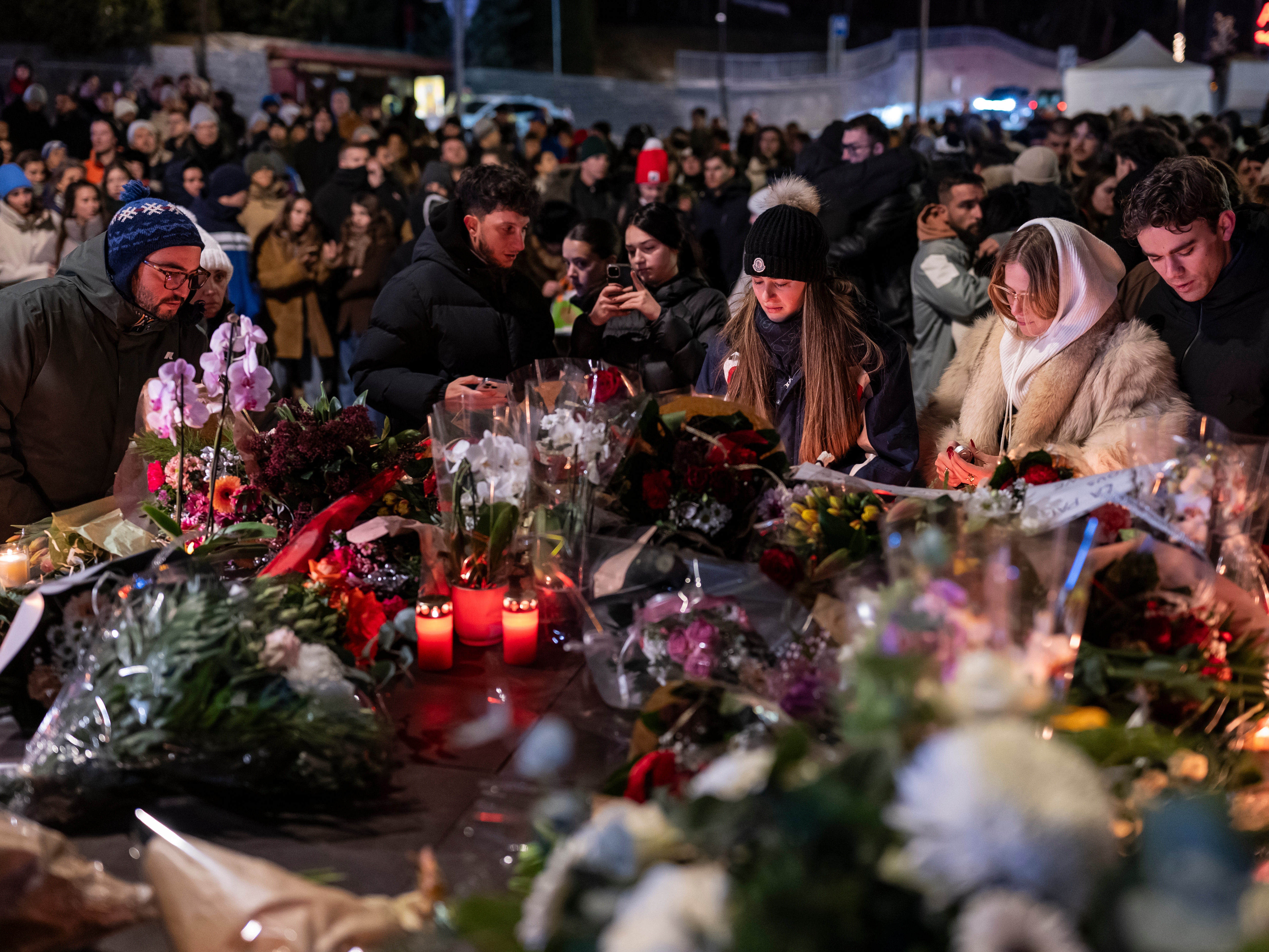 caption: People lay flowers and light candles for the victims of the fire at the "Le Constellation" bar and lounge during New Year's celebration, in Crans-Montana, Switzerland, on Thursday.