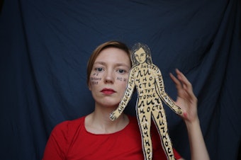caption: A self-portrait of Darya Apakhonchich, with the writing on her face and a figure of a woman saying: "Not only a body but a person, person, person, person, person." She made the photo in support of Russian artist and LGBTQ activist Yulia Tsvetkova, who faces criminal charges for spreading pornography through her art.