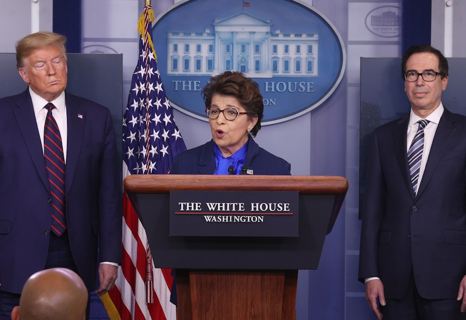 caption: Small Business Administration chief Jovita Carranza speaks at the White House as President Trump and Treasury Secretary Steven Mnuchin look on. Some small business owners are facing delays in applying for a new loan program.