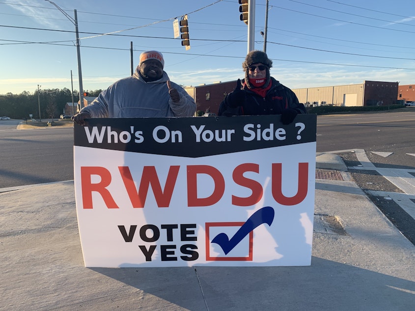 caption: Representatives from the Retail, Wholesale and Department Store Union hold a pro-unionization sign outside Amazon's warehouse in Bessemer, Ala.