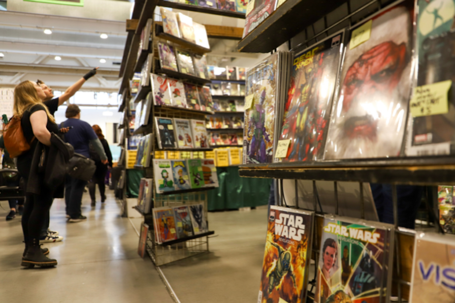 caption: KUOW's Dyer Oxley and Katie Campbell browse a comic book booth at the 2024 Emerald City Comic Con at the Seattle Convention Center. 