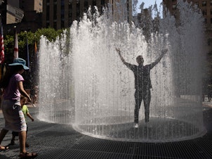 caption: People play in the water-based sculpture of artist Jeppe Hein titled "Changing Spaces" at Rockefeller Center Plaza in New York City on Tuesday.