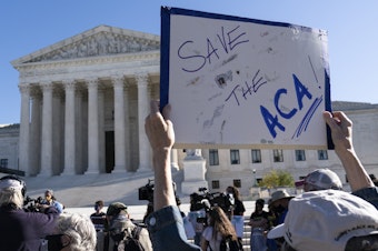 caption: A demonstrator holds a sign in front of the U.S. Supreme Court, which heard arguments over the Affordable Care Act Tuesday.
