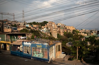 caption: A man cleans a rooftop as the sun sets over the embattled Pedregal neighborhood of Tegucigalpa.
