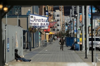 caption: The sidewalk along Alaskan Way in front of Seattle's iconic Ivar's Fish Bar restaurant is nearly empty, Friday, April 10, 2020, as seen from a construction walkway near the Colman Ferry Terminal in Seattle.