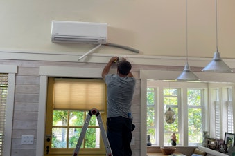 caption: CM Heating technician Hunter Morgan installs a heat pump in a house in Shoreline, Washington, in July 2023.