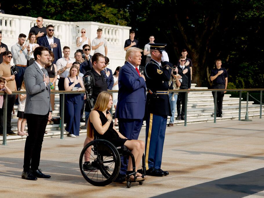 caption: Former President Donald Trump looks on alongside Marlon Bateman (left), Marine Cpl. Kelsee Lainhart and U.S. Marine Corps Sgt. Tyler Vargas-Andrews during a wreath-laying ceremony at Arlington National Cemetery on Aug. 26 to honor the lives of those who died at the Abbey Gate bombing in Afghanistan.
