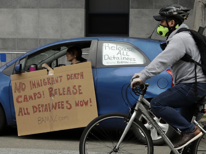 caption: A masked cyclist passes a motorist protesting in a vehicle at a U.S. Immigration and Customs Enforcement field office last month in San Francisco.