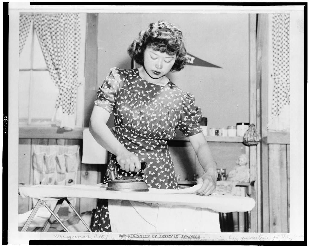caption: Caption by photographer Dorothea Lange: Ester Naite, an office worker from Los Angeles, operates an electric iron in her quarters at Manzanar, California, a War Relocation Authority center where evacuees of Japanese ancestry will spend the duration. 
