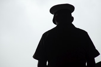 caption: Silhouette of a United States Marine praying, photographed from behind.