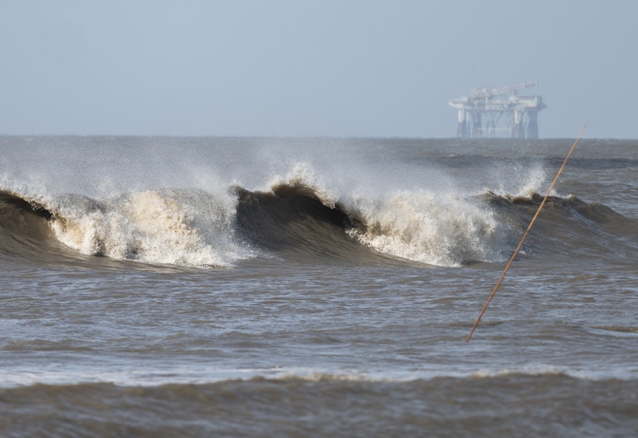 caption: Hurricane Laura sends large waves crashing on a beach in Cameron, La., on Aug. 26 as an offshore oil rig appears in the distance. The most active hurricane season on record was just one of many challenges facing the oil industry this year — aside from the attention-grabbing crisis of the pandemic.