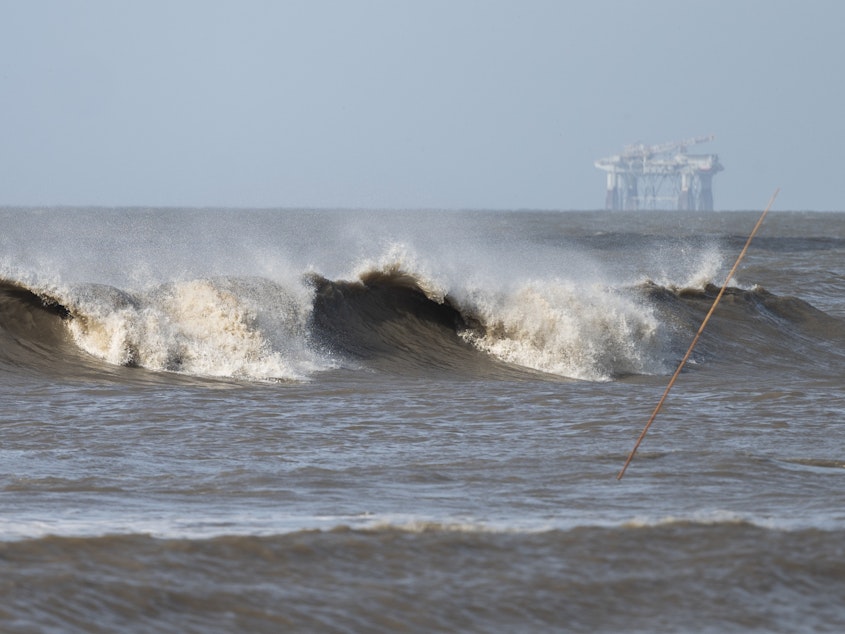 caption: Hurricane Laura sends large waves crashing on a beach in Cameron, La., on Aug. 26 as an offshore oil rig appears in the distance. The most active hurricane season on record was just one of many challenges facing the oil industry this year — aside from the attention-grabbing crisis of the pandemic.