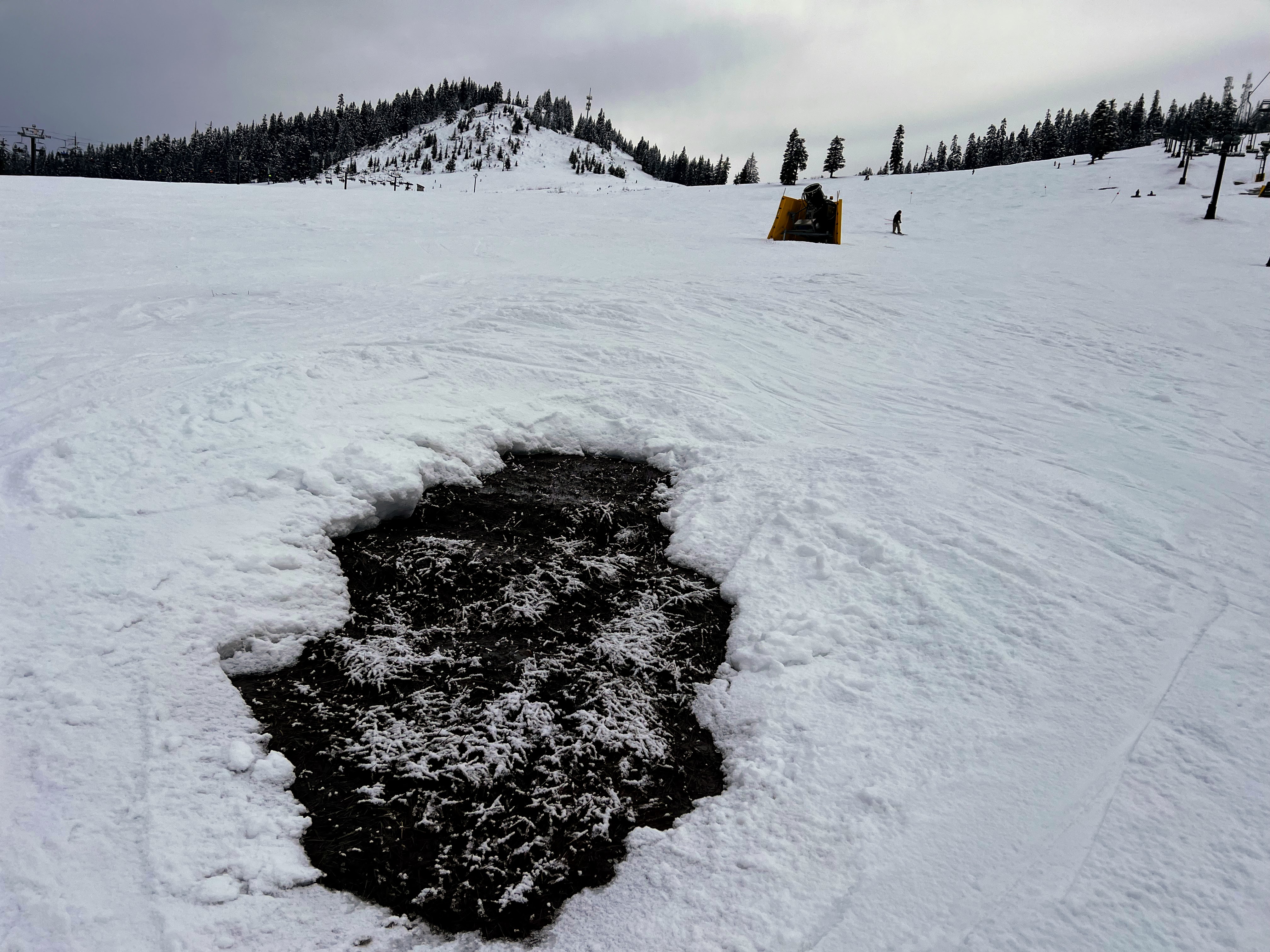 caption: Bare dirt and rocks offered a obstacle course type experience when skiing at Summit at Snoqualmie in February 16th, 2026. In the background, a snow-maker sits idly.