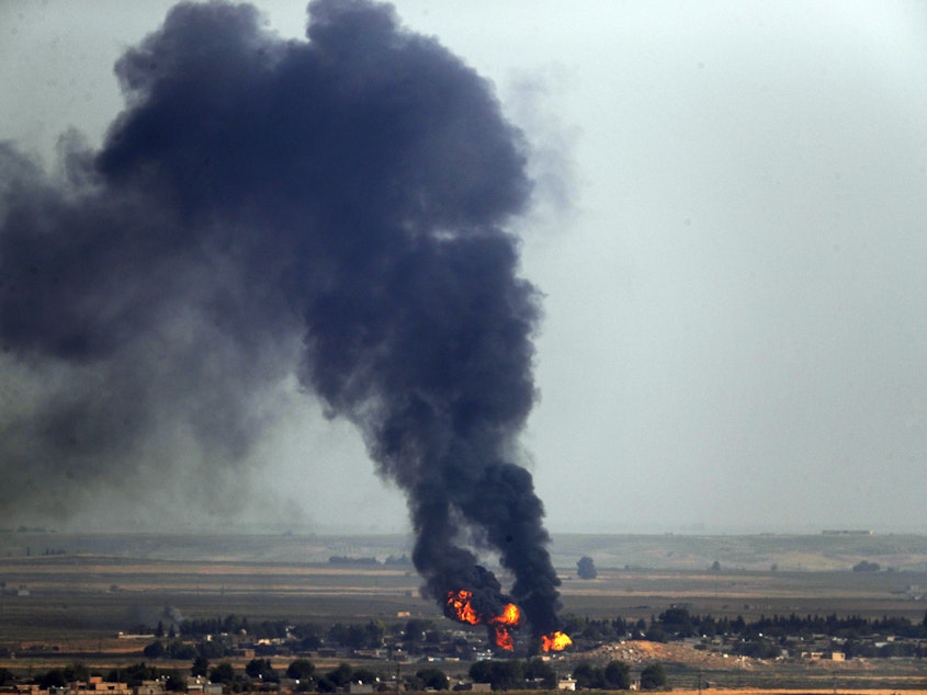 caption: In this photo taken Thursday, flames and smoke billow from a fire on a target in Ras al-Ayn, Syria. This is the result of shelling by Turkish forces, the same day Turkey and the U.S. were negotiating a cease-fire agreement.