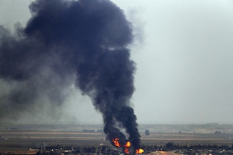 caption: In this photo taken Thursday, flames and smoke billow from a fire on a target in Ras al-Ayn, Syria. This is the result of shelling by Turkish forces, the same day Turkey and the U.S. were negotiating a cease-fire agreement.