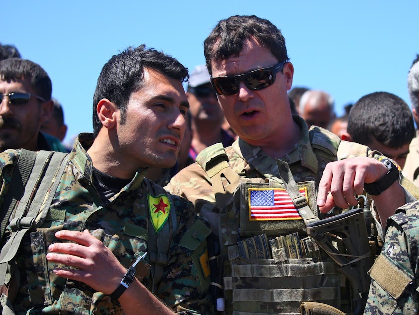 caption: President Trump's plan for the Turkish-Syrian border contradicts recommendations from top officials in the Pentagon and the State Department. In this 2017 photo, a U.S. officer from the coalition against ISIS speaks with a fighter from the Kurdish People's Protection Units (YPG) at the site of Turkish airstrikes near the northeastern Syrian Kurdish town of Derik.
