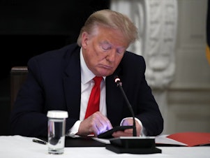 caption: Former President Donald Trump looks at his phone during a roundtable with governors in the State Dining Room of the White House in Washington, June 18, 2020.