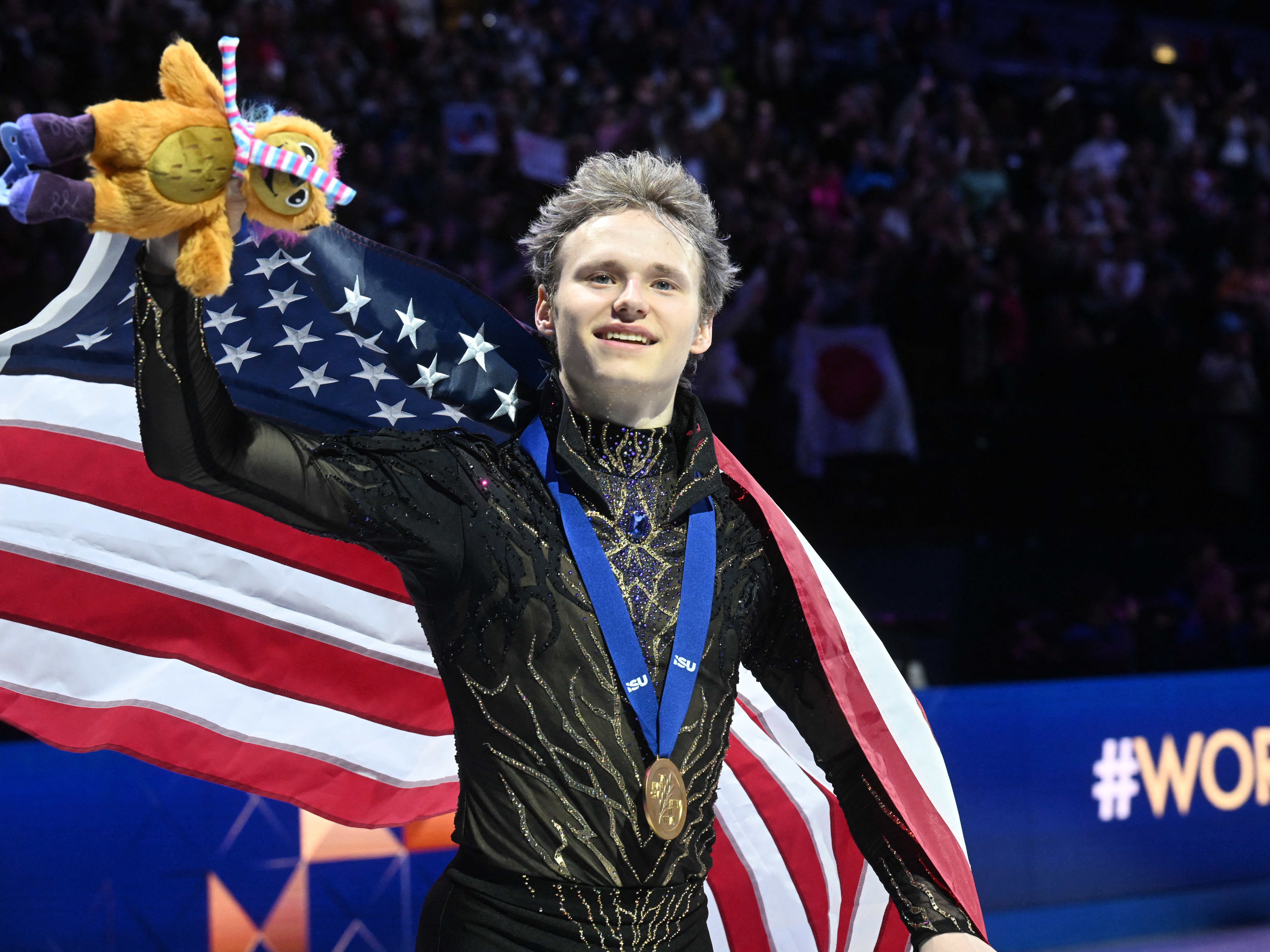 caption: Ilia Malinin celebrates after winning his third Figure Skating World Championships in Prague on Saturday.