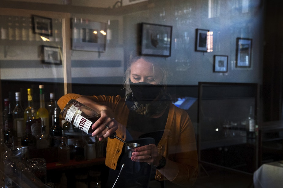 caption: Bartender Cooper Smith makes a drink for a customer behind a sheet of plexiglass on Wednesday, October 21, 2020, at Spinasse on Capitol Hill in Seattle. "We're running with a skeletal staff," said general manager Angela Lopez, "but there are still people here who are putting themselves at risk." 