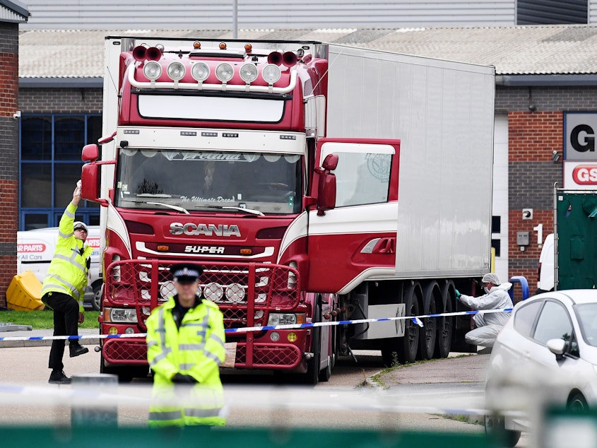 caption: Police and forensic officers investigate a truck and refrigerated trailer where 39 bodies were discovered in Thurrock, England.