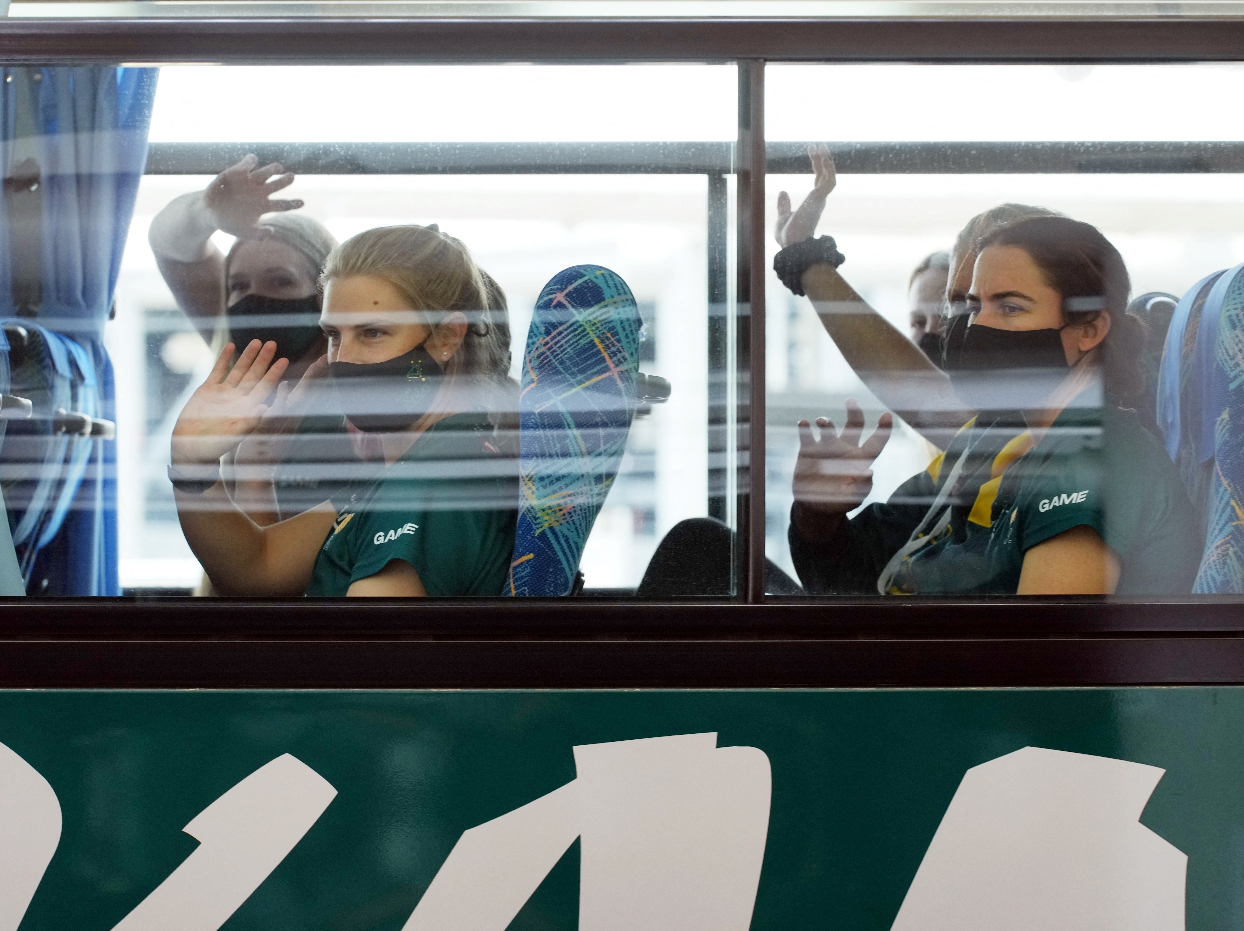caption: Australian softball players, the first foreign team to arrive for the Tokyo Olympic Games, wave from their bus after arriving at Narita International Airport on June 1.