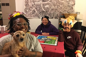 caption: Mattie Mooney (L with dog Zoe) and family Nanta (C) and Zaiya Rylee (R) pose around the board game Sorry. About this photo, Mooney wrote: "Please disregard the eyebrows my kid and roommate drew on the dog as if she didn’t look concerned enough without them."