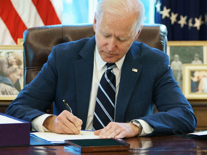 caption: President Biden signs the American Rescue Plan Thursday in the Oval Office. The $1.9 trillion economic stimulus bill includes $1,400 stimulus checks for most Americans.