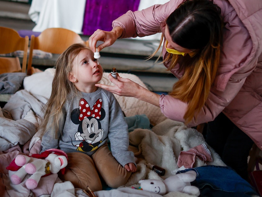 caption: Ukrainian refugee Alina Archipova gives her daughter medication at a temporary shelter in Berlin, Germany, on March 10.