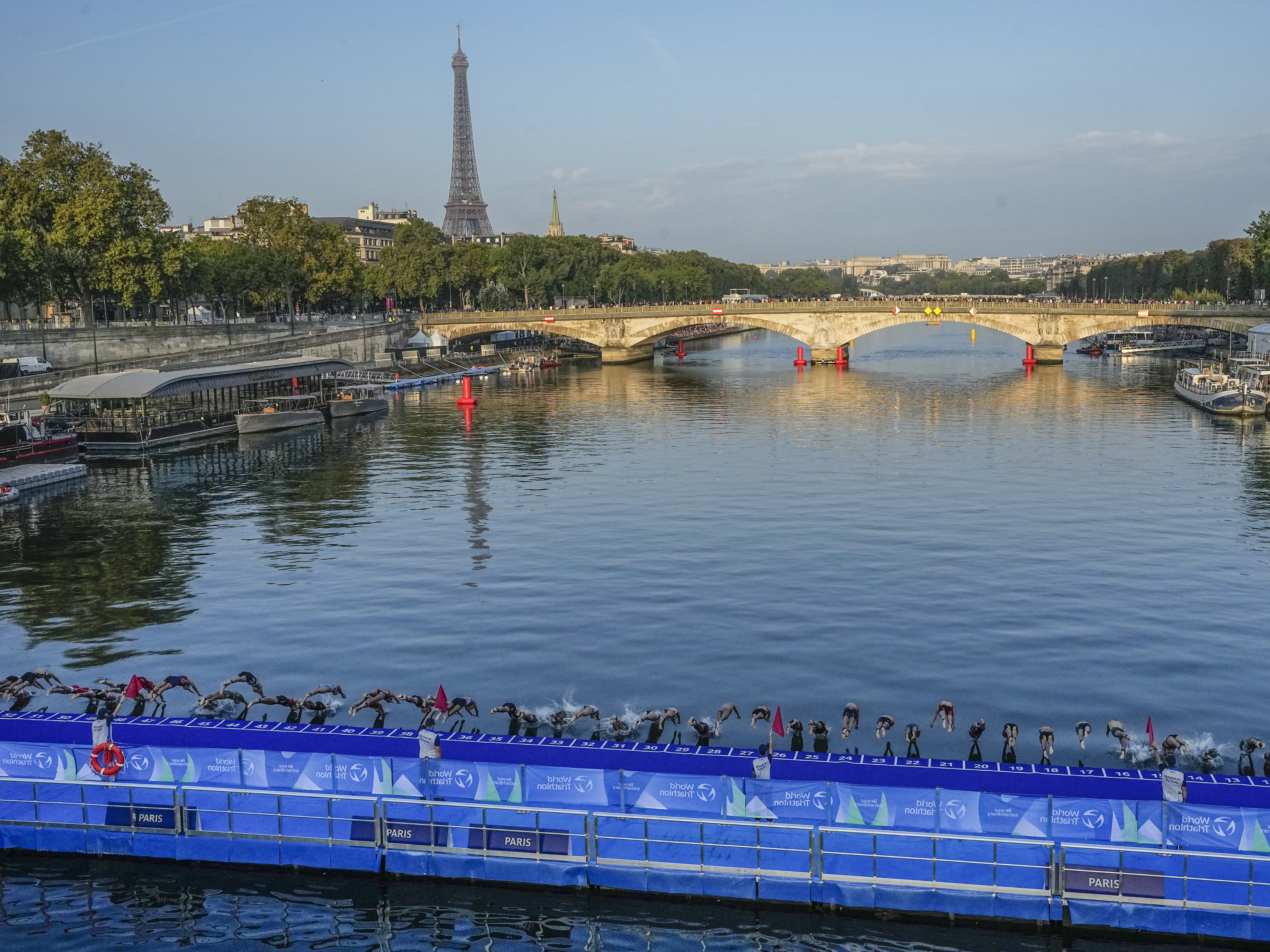 caption: Athletes dive into the Seine River from the Alexander III bridge on the start of the first leg of the women's triathlon test event for the 2024 Paris Olympics in Paris in August 2023.