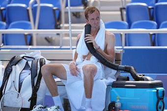 caption: Daniil Medvedev cools down during the break with air from a mobile air conditioner and a towel with ice cubes at the Tokyo Olympics.