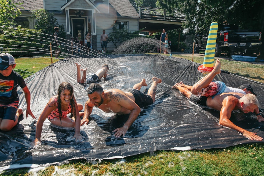 caption: Vasili Vouros, center, and John Cain Jr., right, slip n' slide with their kids in Vouros's front yard in Skyway, Monday, June 28. The National Weather Service recorded 108 degrees in SeaTac on Monday, setting an all-time record for the area. A car temperature gauge recorded 109 degrees in Skyway at 4:30 pm.
