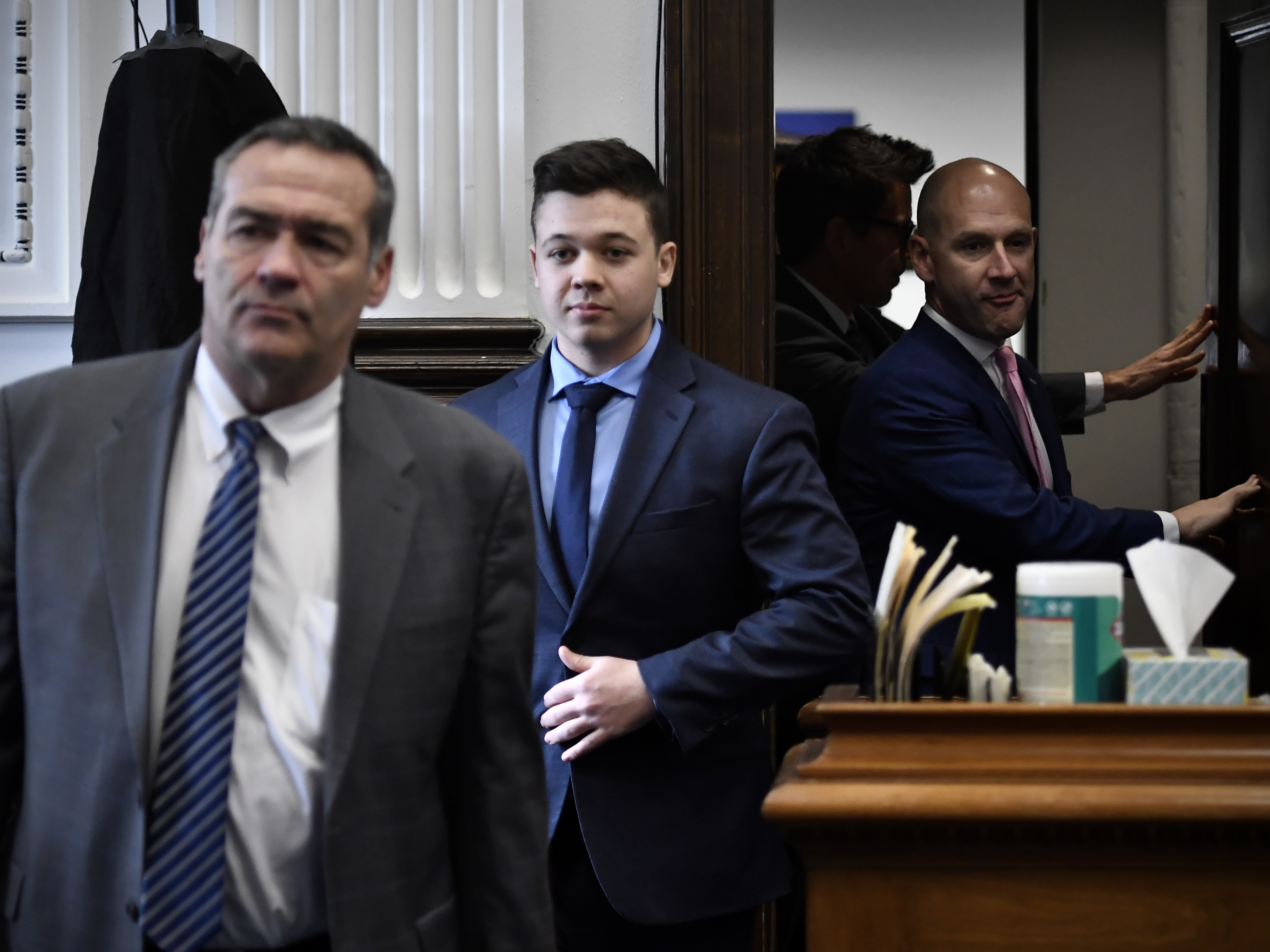 caption: Kyle Rittenhouse, center, enters the courtroom with his attorneys Mark Richards, left, and Corey Chirafisi.