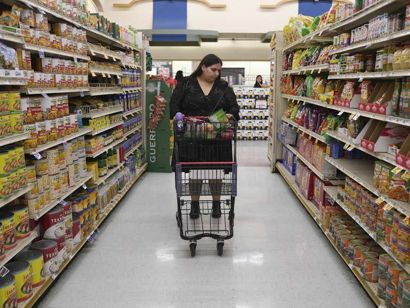 caption: Jaqueline Benitez pushes her cart down an aisle as she shops for groceries at a supermarket in Bellflower, Calif., on Monday, Feb. 13, 2023. Benitez, 21, who works as a preschool teacher, depends on California's SNAP benefits to help pay for food.