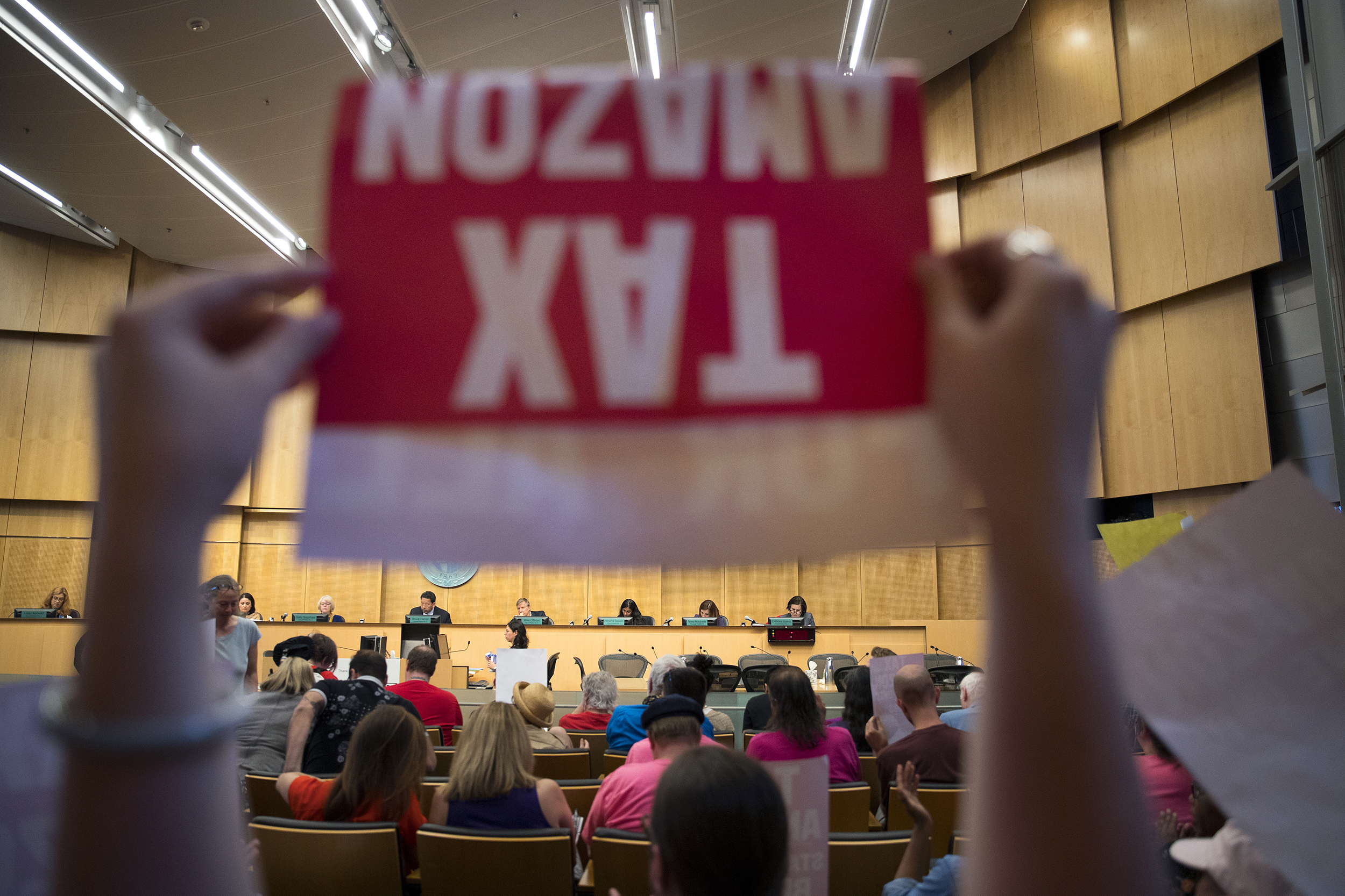 caption: Caitlin Lee raises a Tax Amazon sign in front of Seattle City Council members on Monday, May 14, 2018, during a head tax vote at City Hall in Seattle. 