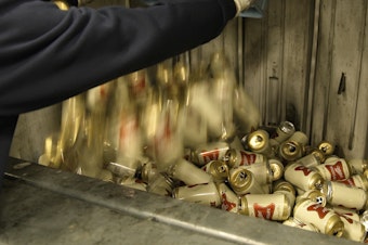 caption: A worker dumps empty cans of Miller High Life beer into a machine to be crushed at the Westlandia plant in Ypres, Belgium, on Monday.