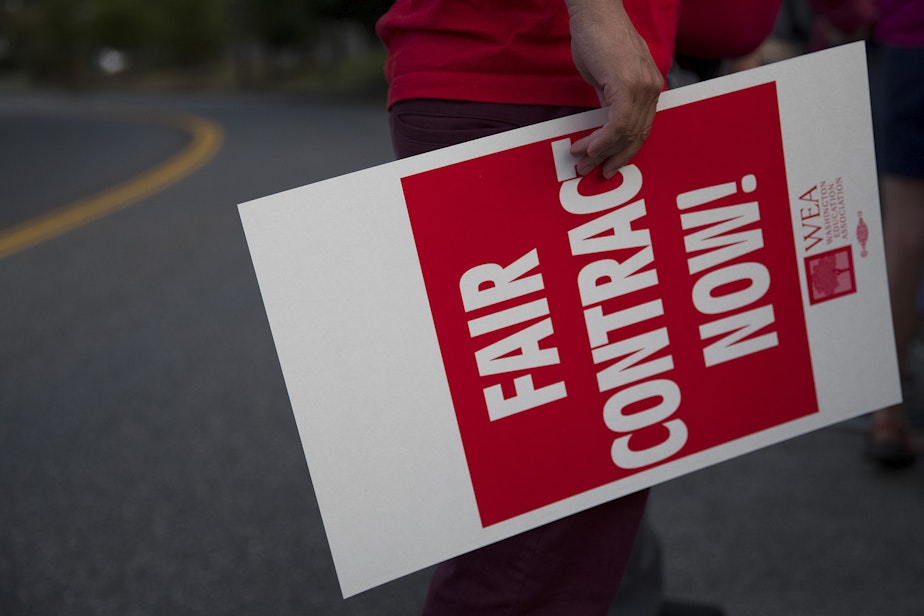 caption: Dan Bremson, a teacher at McClure Middle School, holds a Fair Contract Now sign on Wednesday, August 14, 2019, on the I-5 N. 117th Street overpass in Seattle.