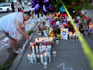 caption: On Sunday, a woman lights a candle at a makeshift memorial to the victims of Saturday's mass shooting at Tops market in Buffalo, N.Y.