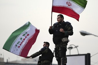 caption: Two anti-riot police officers wave the Iranian flags during a street celebration after Iran defeated Wales in Qatar's World Cup, at Sadeghieh Sq. in Tehran, Iran, Friday, Nov. 25, 2022.