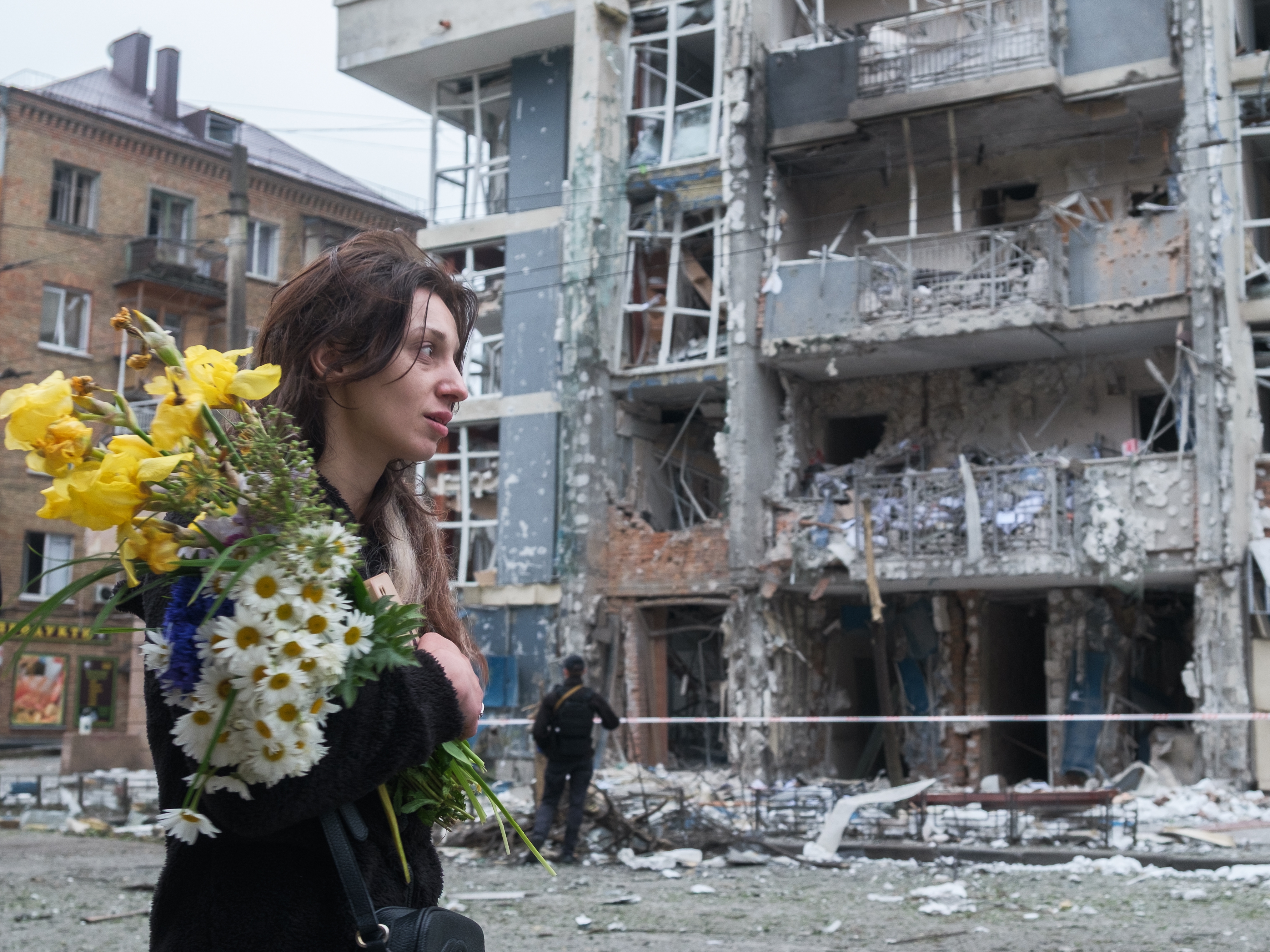 caption: A woman with a bouquet of flowers walks past a high-rise residential building heavily damaged by a Russian drone strike in the Shevchenkivskyi district of Kyiv, Ukraine, on May 25, 2025.