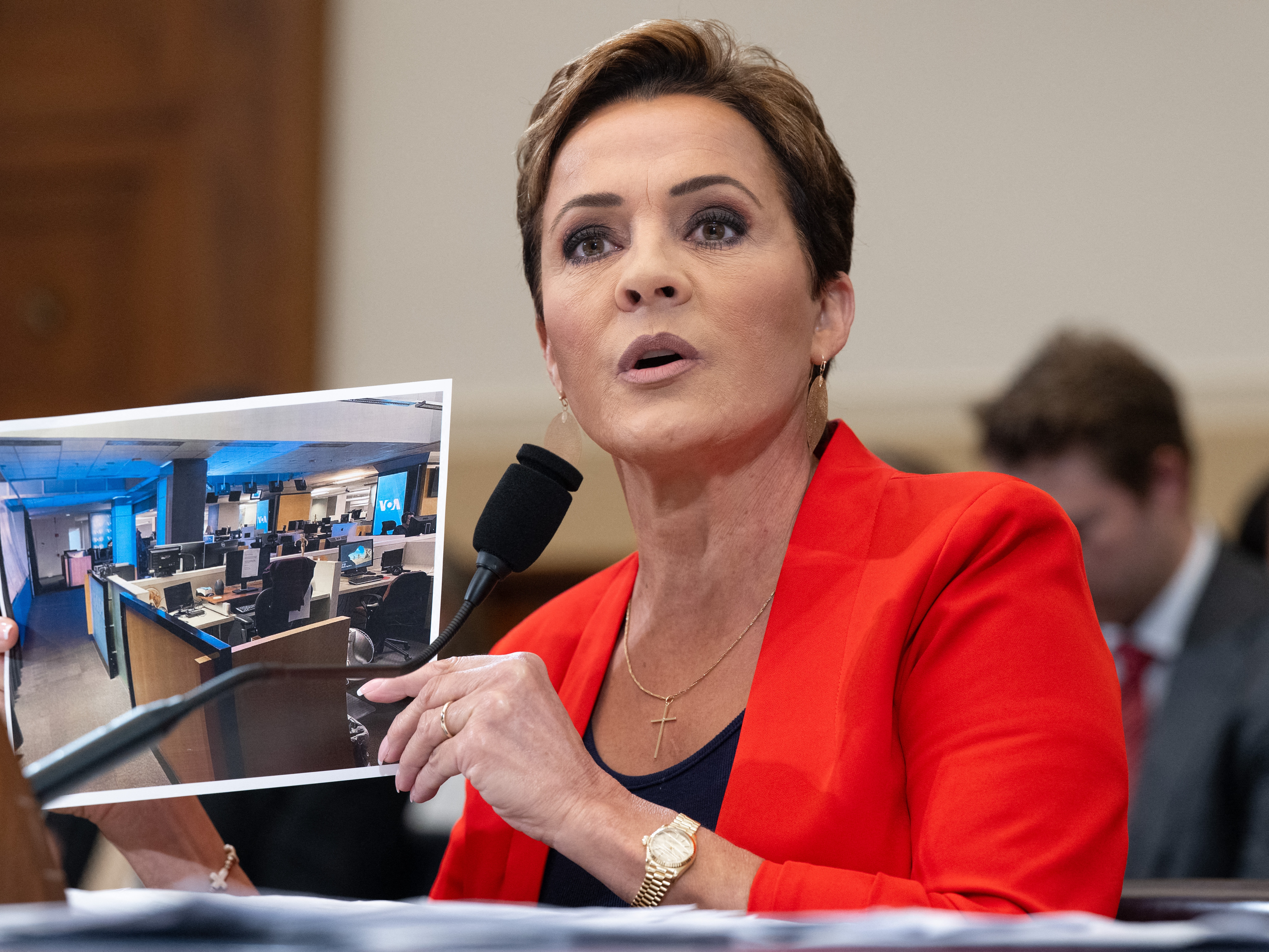 caption: Kari Lake, who led Voice of America's parent agency for the past year, holds up a photo of the international broadcaster's newsroom during a House Foreign Affairs Committee hearing on June 25, 2025.