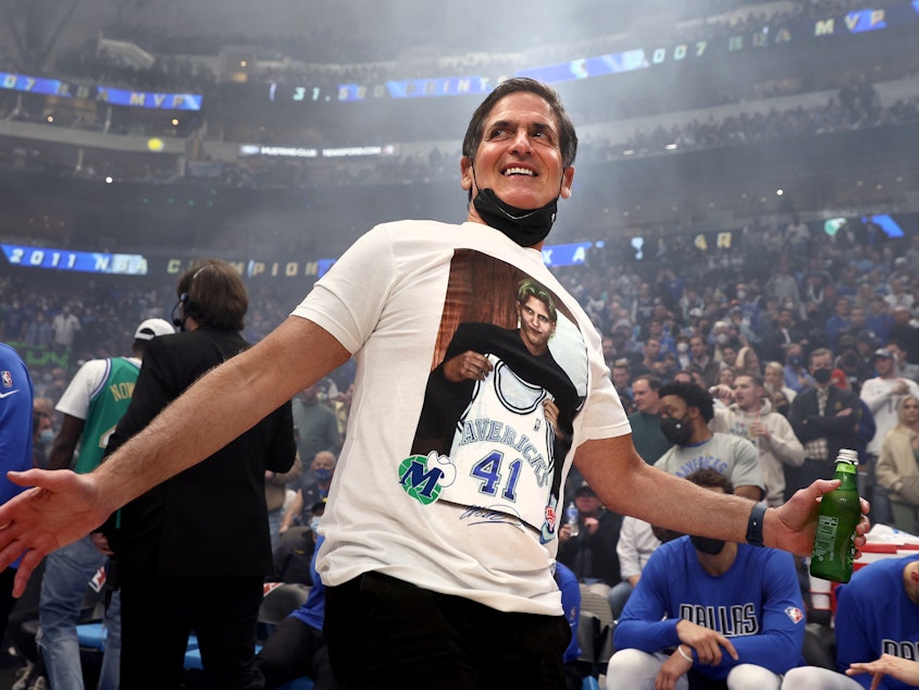 caption: Dallas Mavericks owner Mark Cuban wears a shirt honoring former player Dirk Nowitzki during a ceremony honoring Nowitzki's career on Jan. 5, 2022 in Dallas.