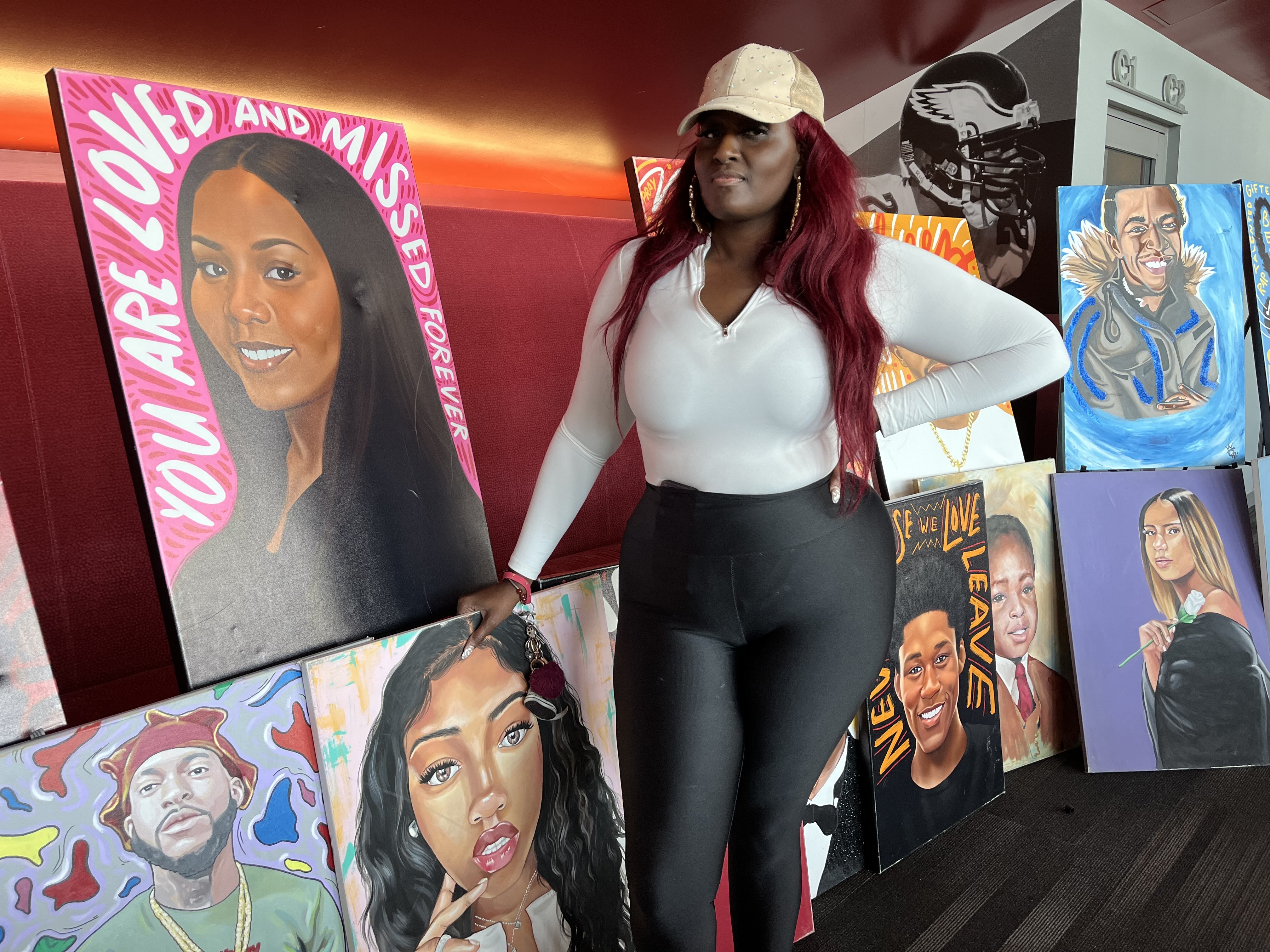 caption: Zarinah Lomax stands beside portraits she commissioned, mostly of young people who died from gunfire. “The purpose is not to make people cry,” Lomax says. “It is for families and for people who have gone through this to know that they are not forgotten.” 