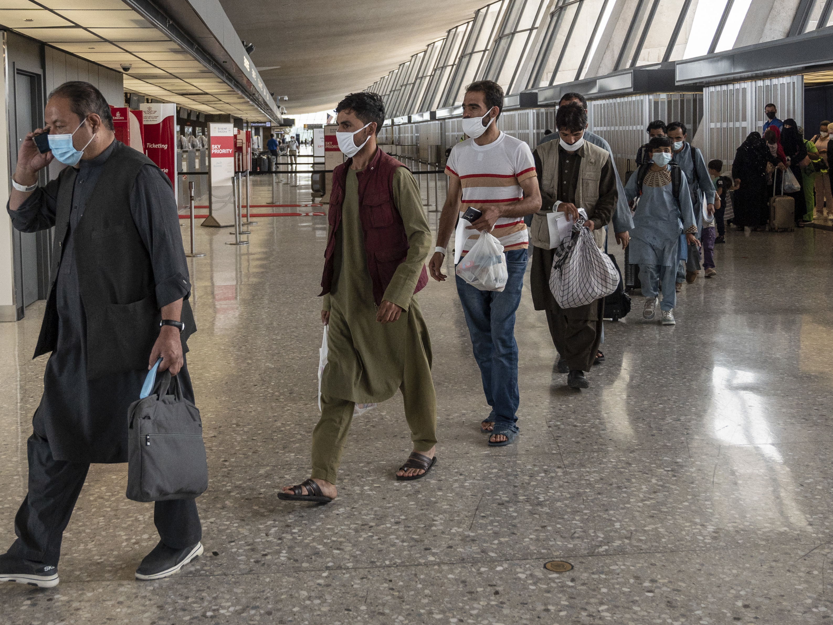 caption: Refugees from Afghanistan are escorted to a bus after arriving and being processed Monday at Dulles International Airport in Virginia. The federal government is reportedly offering COVID-19 vaccines for Afghan arrivals at a site near the airport.