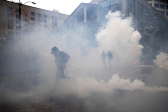 caption: Thousands gathered in protest following the murder of George Floyd on Saturday, May 30, 2020, in Seattle. Here, protesters run from tear gas and flash bang grenades deployed by Seattle police officers near Westlake Park. For over 150 consecutive days, protesters demanding racial justice and an end to police brutality continued to march in Seattle.