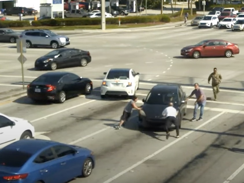 caption: People help a driver who is experiencing a medical episode in Boynton Beach, Fla., on May 5.