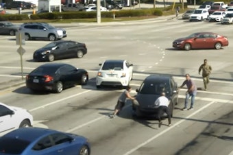 caption: People help a driver who is experiencing a medical episode in Boynton Beach, Fla., on May 5.