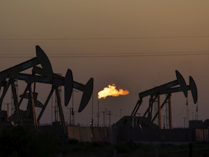caption: A flare burns off methane and other hydrocarbons as oil pumpjacks operate in the Permian Basin in Midland, Texas. Burning fossil fuels like coal, oil and natural gas is the main driver of global warming.