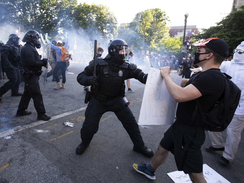 caption: A law enforcement officer raises a baton and tear gas is fired during protests near the White House on June 1.
